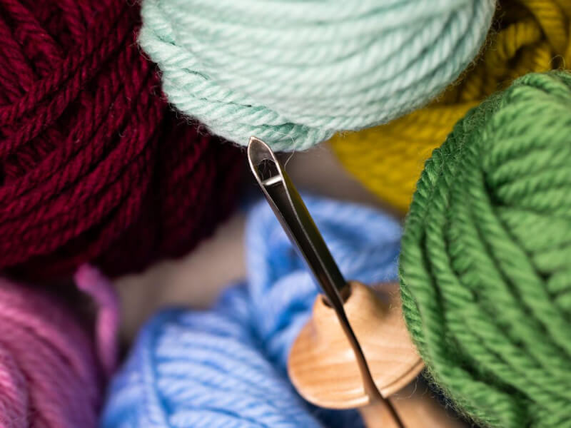 close up of a punch embroidery needle surrounded by balls of coloured yarn